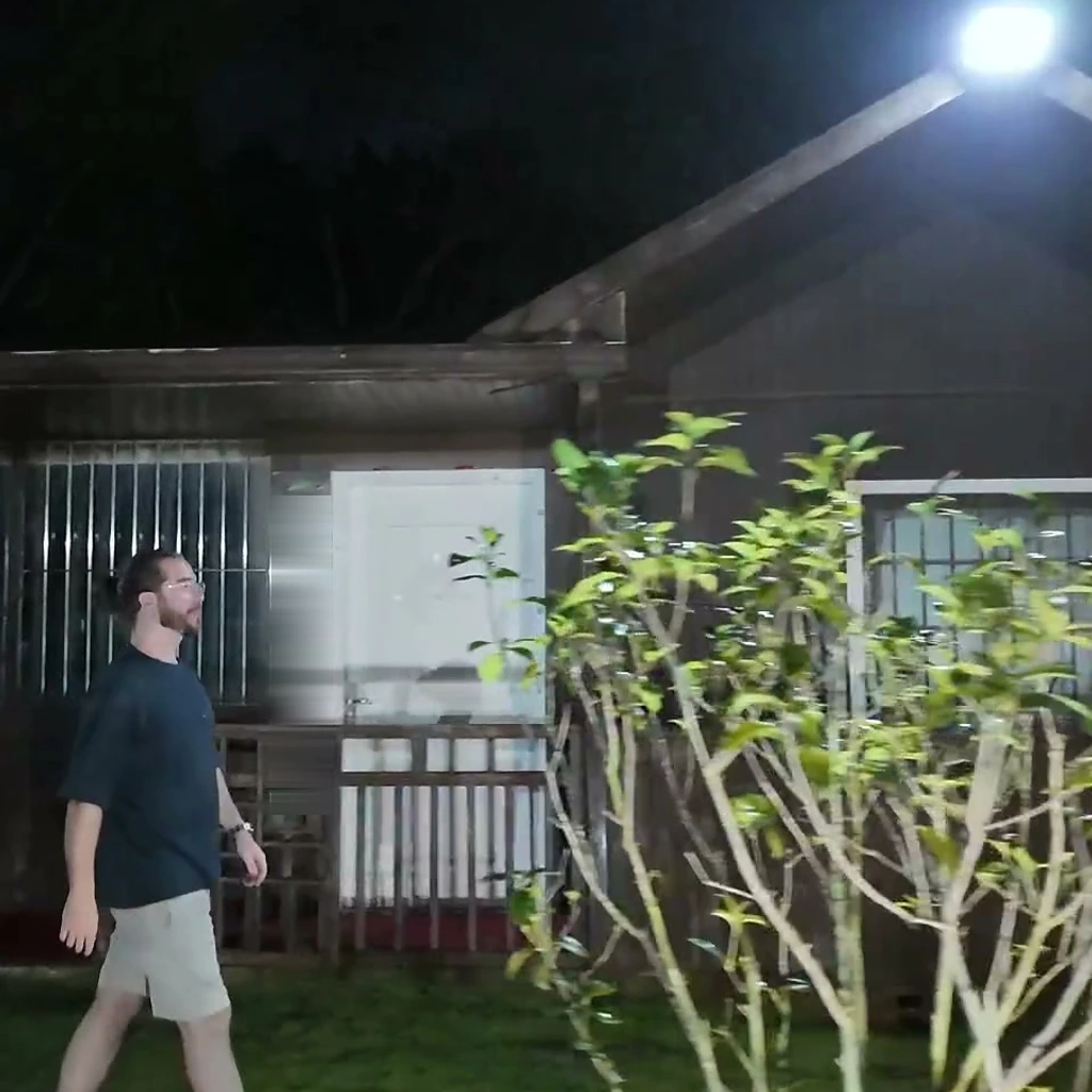De noche el foco del tejado se enciende al máximo e ilumina como de día a un hombre que cruza el patio